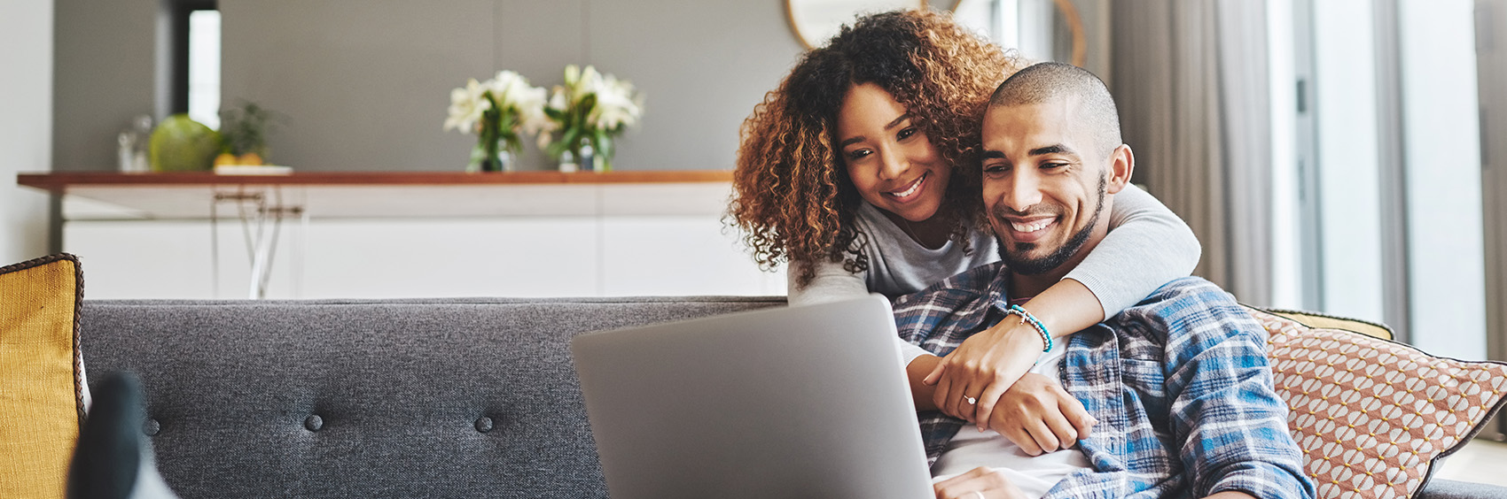 "Man working on laptop while woman hugs him"