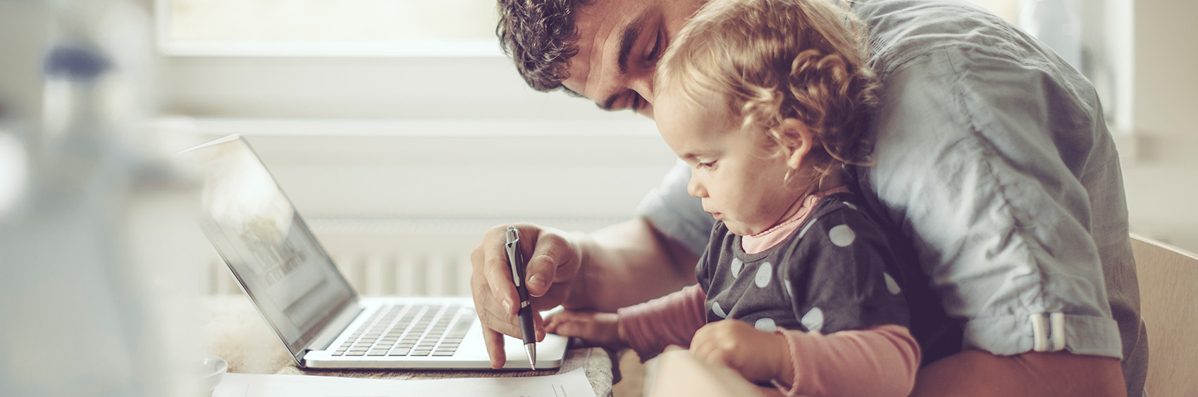 "Man working on laptop while holding a child"