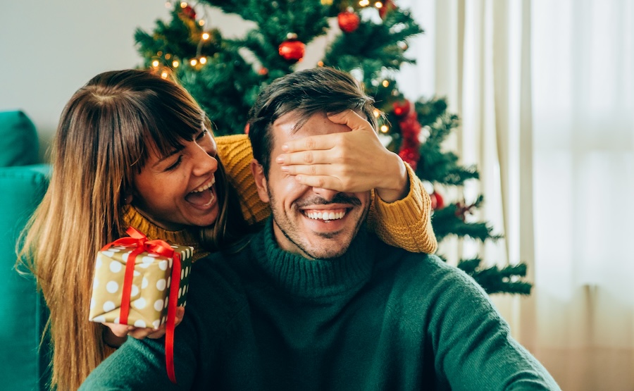 woman gifting man christmas present, gift yourself a new smile this Christmas with teeth whitening, veneers, Invisalign, dental implants, or crowns